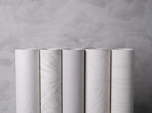 Rouleaux de papier peint clair devant un mur recouvert d'un papier peint à motifs de nuages
